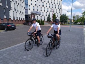 dwóch policjantów na rowerach jedzie po parkjingu Komendy Miejskiej w Częstochowie