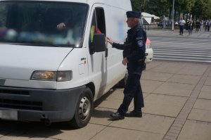 policjant stoi przy białym samochodzie i rozmawia przez otwartą szybę z kierowcą