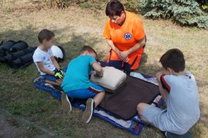 3 chłopców uczy się udzielania pierwszej pomocy przy ratowniku medycznym
