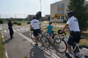 policjanci na rowerach jeżdżą z dziećmi po miasteczku rowerowym