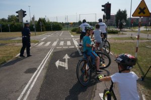 dwóch policjantów na rowerach jeździ po miasteczku rowerowym z dziećmi na rowerach