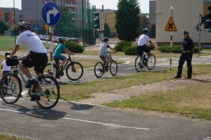 dwóch policjantów na rowerach jeździ po miasteczku rowerowym z dziećmi na rowerach