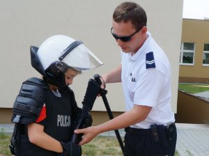 policjant pomaga chłoipczykowi założyć kamizelkę kuloodporną