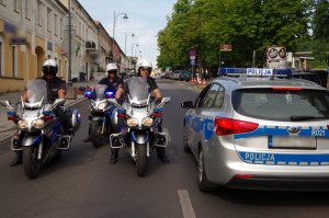 trzech policjantów na motocyklach służbowych stoją obok radiowozu na ulicy