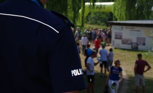 rękaw koszuli policjanta z napisem policja a w tle miejsce startu zawodników