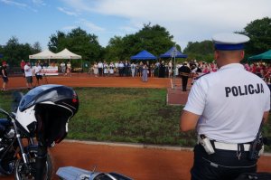 policyjny motocyklista stoi tyłem do fotografującego, w tle goście uroczystości