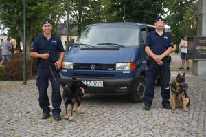 policyjni przewodnicy z psami służbowymi stoją przy samochodzie