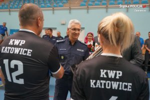 policjant składajacy uścisk dłoni, tyłem do zdjecia kobieta i mężczyzna w koszulce z napisem KWP Katowice