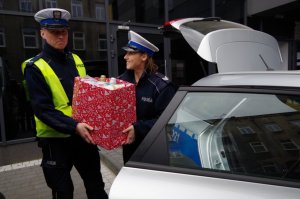 policjantka z policjantem wynoszą pudełka z zabawkami z radiowozu