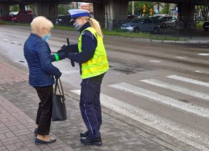 policjantka przy przejściu dla pieszych rozdaje pieszym opaski odblaskowe