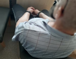 mężczyzna z założonymi kajdankami na ręce siedzi na krześle