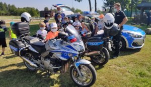 policyjny radiowóz i motocykle na trawie, w tle dzieci - uczestnicy półkolonii