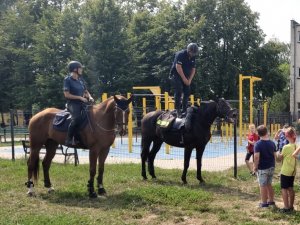 policjanci na koniach służbowych stoją przed grupą dzieci