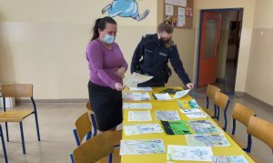 policjantka i nauczycielka podczas oceniania prac rozłożonych na stolikach w szkole