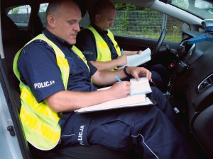 policjanci z drogówki piszą w swoich notatnikach siedząc w radiowozie