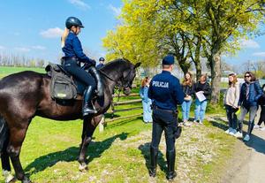 policjanci na koniach stoją na trawie, przed nimi grupa osób przygląda się im