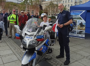policjant pozuje do zdjęcia przy motocyklu, na którym siedzi chłopiec