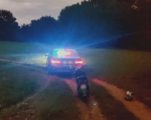 policyjny nieoznakowany radiowóz z włączonymi sygnałami uprzywilejowania stoi na polnej drodze, z anim ustawiony motorower