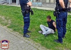 Na zdjęciu policjanci i mężczyzna siedzący na trawie.